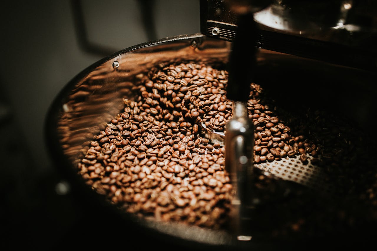 services-04 Close-up of freshly roasted coffee beans in a large industrial coffee roaster, showcasing rich textures and warm tones.